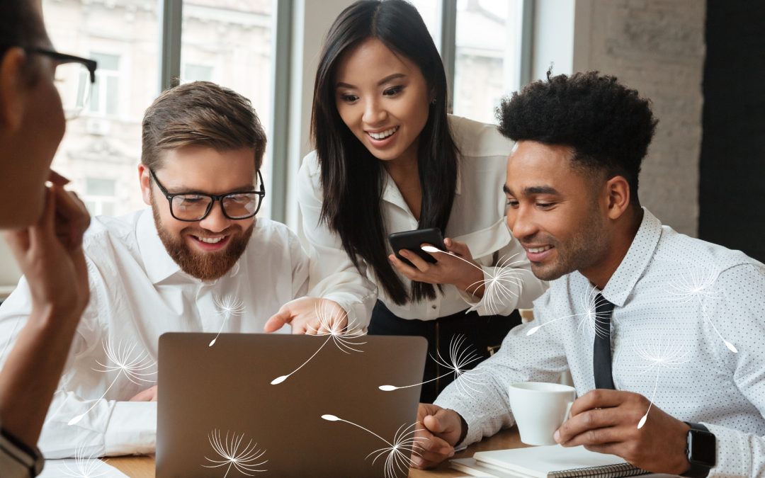 A diverse group of young professionals smiling and collaborating around a laptop in a modern office setting. One person holds a phone, another holds a coffee cup, and stylized white dandelion seeds are overlaid on the image, adding a light, creative touch.