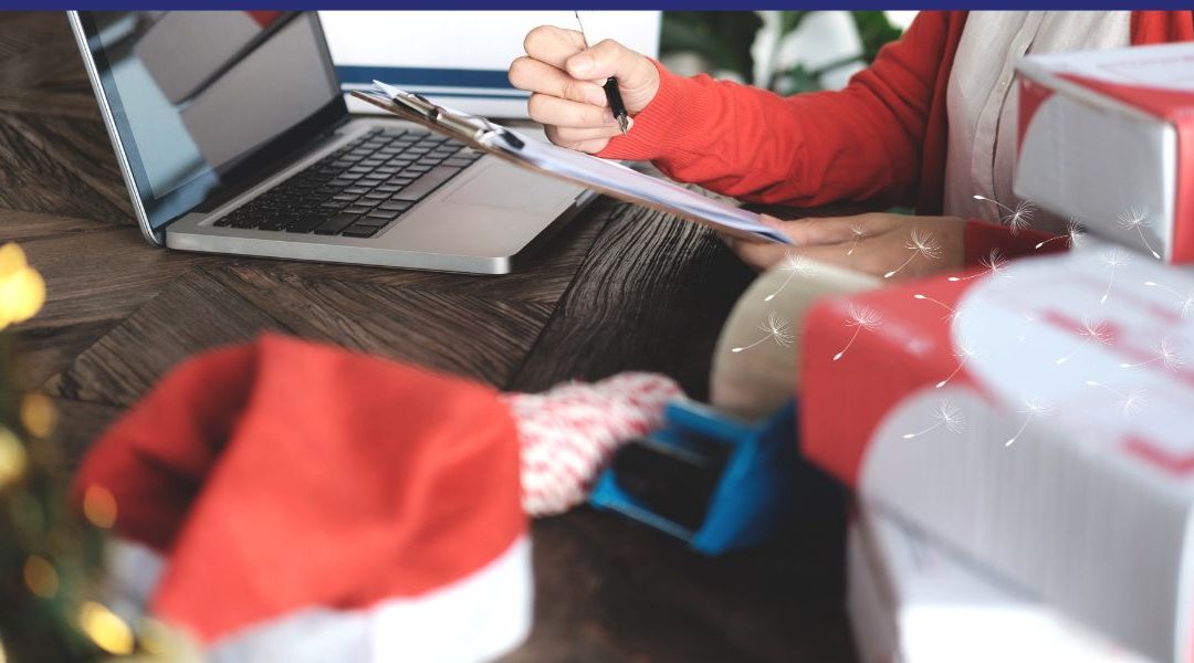A person in a red sweater sits at a wooden table working on a laptop and writing on a clipboard. Holiday shipping boxes, red-and-white twine, tape, and a Santa hat are on the table. Soft dandelion illustrations float across the image, adding a light, festive feel.