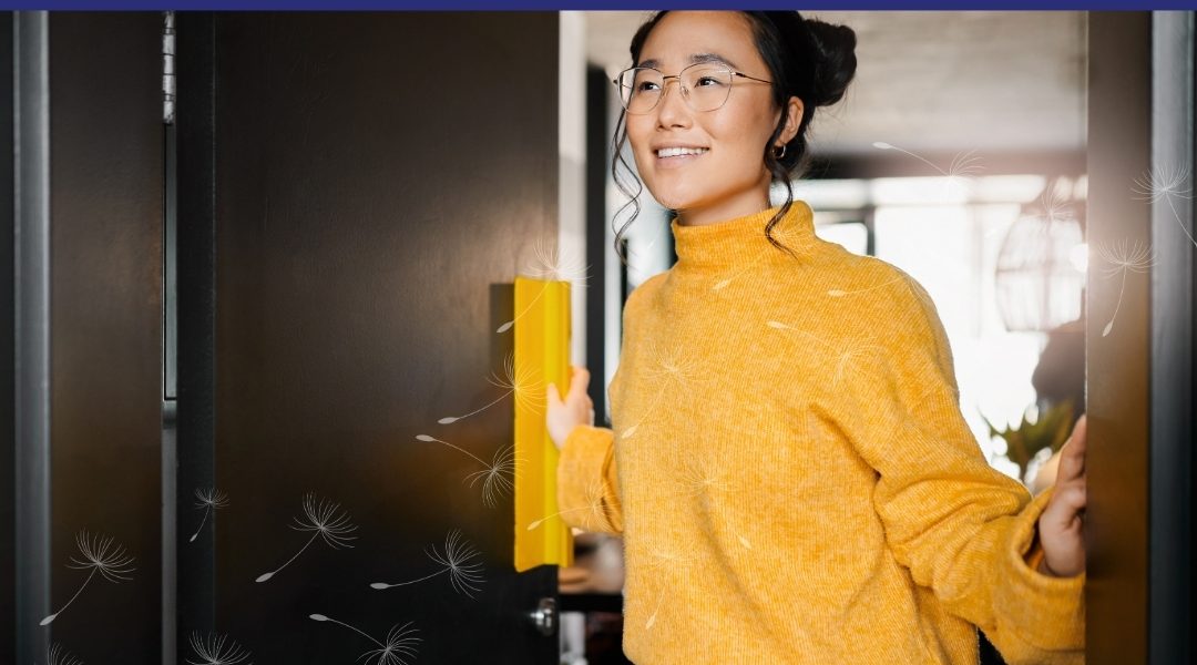 A woman wearing glasses and a yellow sweater opens a door and smiles as she steps into a bright room. Soft dandelion seed graphics float across the image.